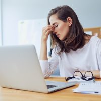 Beautiful stressed young office worker sitting at desk holding head because of pain in office