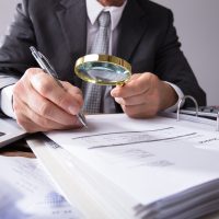 Businessperson Looking At Receipts Through Magnifying Glass Businessperson Looking At Receipts Through Magnifying Glass