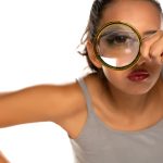 a suspicious young woman looks through a magnifying glass