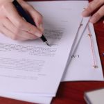 Closeup of a hand signing a last will by a pen.