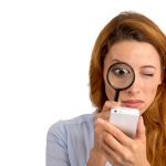 woman looking through magnifying glass at smart phone