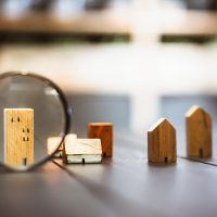 Hand holding magnifying glass and looking at house model, house